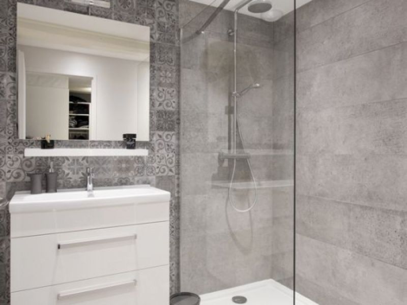 Baño con azulejos en tono gris, plato de ducha y sanitarios de color blanco